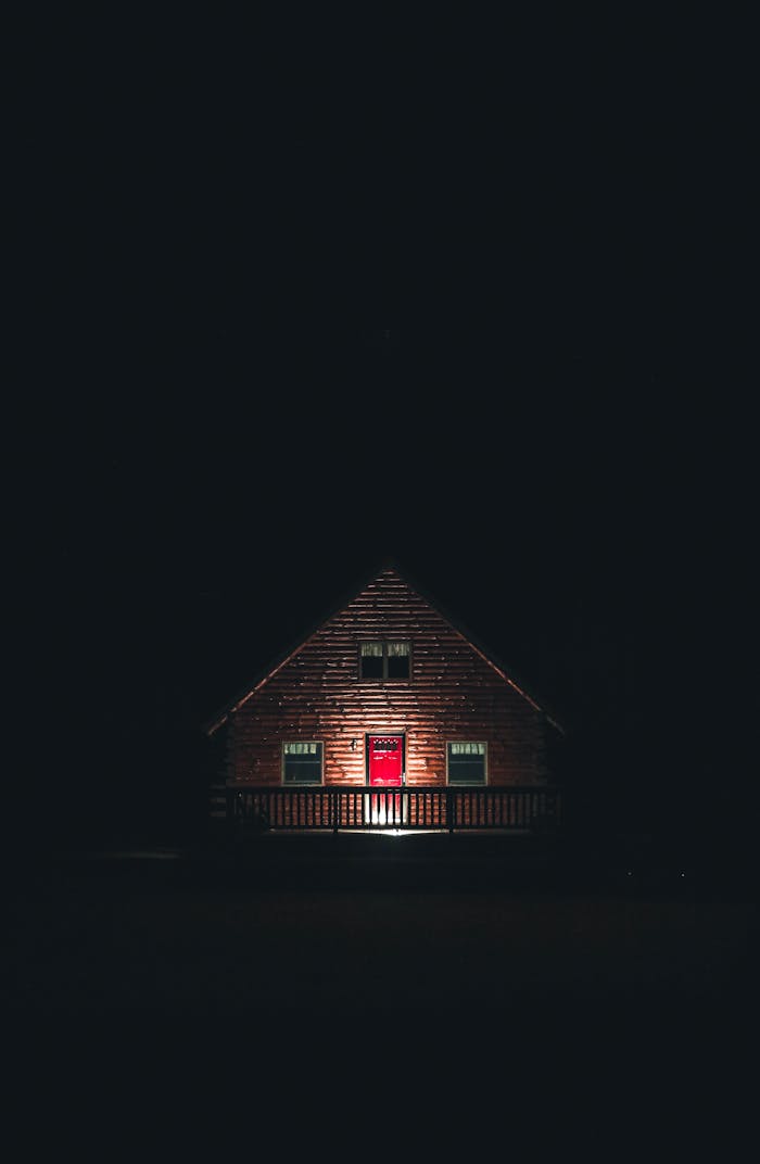 gallery-4 A captivating wooden house with a red door, illuminated at night in a moody setting. Perfect for architectural and real estate themes.